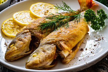 Fried perch with lemon and salad served on wooden table
