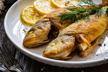 Fried perch with lemon and salad served on wooden table
