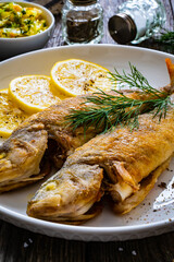 Fried perch with lemon and salad served on wooden table
