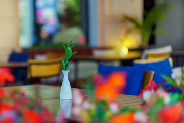 White thin vase with green plant on a table in a restaurant