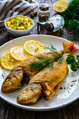 Fried perch with lemon and salad served on wooden table
