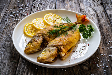 Fried perch with lemon and salad served on wooden table

