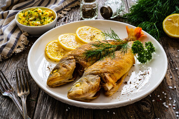 Fried perch with lemon and salad served on wooden table
