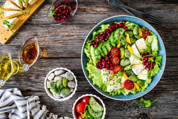 Tasty salad - leafy greens, camembert, pear,  pomegranate, cherry tomatoes and broad bean on wooden table
