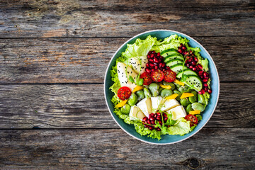 Tasty salad - leafy greens, camembert, pear,  pomegranate, cherry tomatoes and broad bean on wooden table
