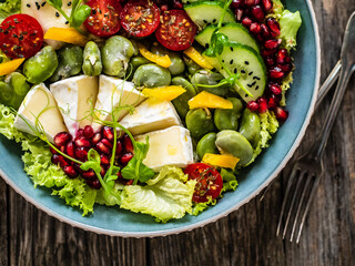 Tasty salad - leafy greens, camembert, pear,  pomegranate, cherry tomatoes and broad bean on wooden table
