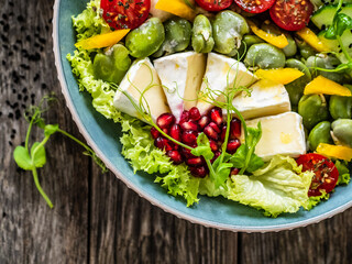 Tasty salad - leafy greens, camembert, pear,  pomegranate, cherry tomatoes and broad bean on wooden table
