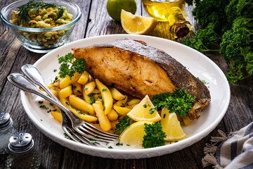 Fish dish - fried halibut with French fries and lemon on wooden table
