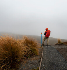 Hiking Tama Lakes track in thick fog and rain, among golden and red tussocks. Tongariro National...