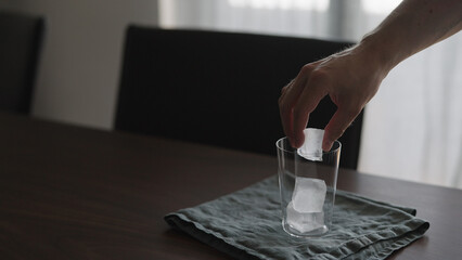 Fototapeta na wymiar man put ice into tumbler glass on wood table