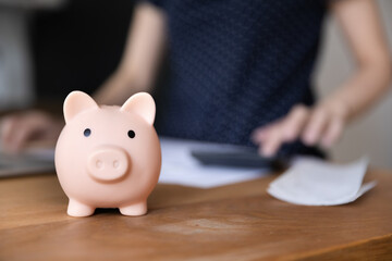 Obraz na płótnie Canvas Piggy bank for saving money on table close up. Accountant woman, finance professional counting money, checking paper financial reports, using calculator in background. Business, investment concept