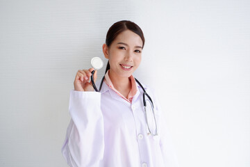 A smiling, beautiful Asian female doctor puts a stethoscope on her shoulder. wearing a white robe on a white background.