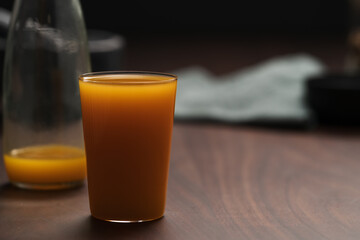 orange, pumpkin and carrot mixed juice in tumbler glass on walnut table
