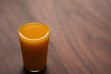 orange, pumpkin and carrot mixed juice in tumbler glass on walnut table