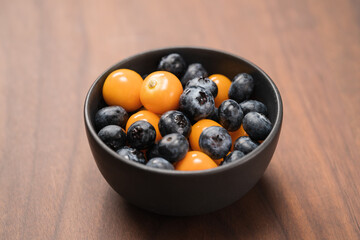 Blueberries with physalis in a bowl on wood table