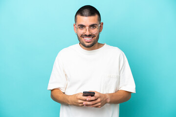 Young caucasian man isolated on blue background sending a message with the mobile