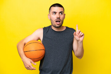 Young caucasian basketball player man isolated on yellow background thinking an idea pointing the finger up