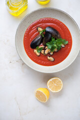 Plate of tomato cream-soup with mussels over beige marble background, vertical shot with space, view from above