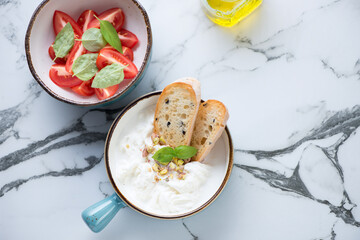 Turquoise bowls with stracciatella di bufala and red tomatoes, above view on a black and white marble background, horizontal shot with space