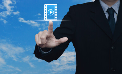 Businessman pressing play button with movie flat icon over blue sky with white clouds, Business cinema online concept