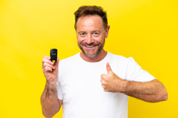 Middle age caucasian man holding car keys isolated on yellow background with thumbs up because something good has happened