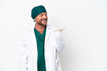 Middle age surgeon in green uniform isolated on white background pointing to the side to present a product