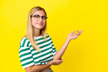 Blonde Uruguayan girl isolated on yellow background extending hands to the side for inviting to come
