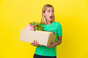 Fototapeta na wymiar Young Uruguayan girl making a move while picking up a box full of things isolated on yellow background looking up and with surprised expression