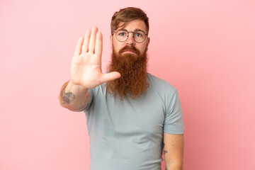 Young reddish caucasian man isolated on pink background making stop gesture