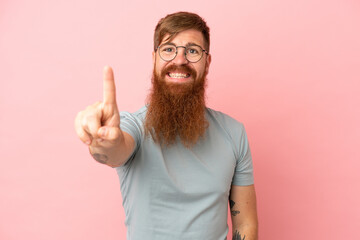 Young reddish caucasian man isolated on pink background showing and lifting a finger