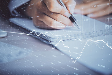 A woman hands writing information about stock market in notepad. Forex chart holograms in front. Concept of research. Multi exposure