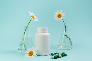 A bottle of pills on a blue background. Flasks with medicinal plants. Place for text. Medical concept photo. Chamomile and pills