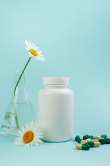 A bottle of pills on a blue background. Flasks with medicinal plants. Place for text. Medical concept photo. Chamomile and pills