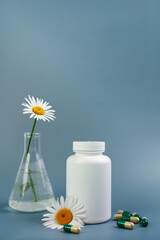 A bottle of pills on a blue background. Flasks with medicinal plants. Place for text. Medical concept photo. Chamomile and pills