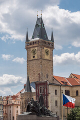 Old Town Hall with ancient clock in historical downtown Prague. Tower of Staromestska Radnice, flag of Czech Republic, Monument by Jan Hus and Medieval buildings around.