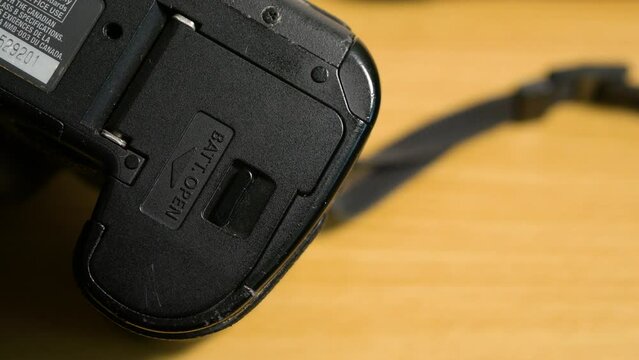 The photographer inserts the battery into the compartment of the SLR camera, close-up, selective focus
