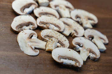 white champignons sliced on slides on a wooden cutting board background