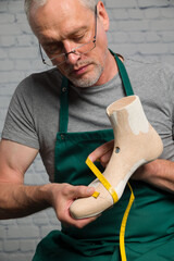 shoemaker wearing a green apron is doing qualitity control at an individual made wooden last to make an individual crafted orthopedic shoe