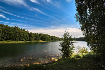 Naklejka premium Beautiful lakeside view from a small lake in Russia, with lush green trees, blue sky and sunlight