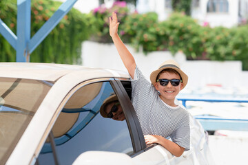 Happy smilind Caucasian little boy in hat and sunglasses sitting in white automobile. Car road trip. Traveling by auto. summer vacation concept.