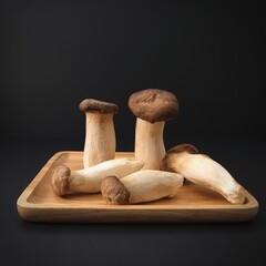 Popular uncooked healthy asian edible King Oyster mushrooms on wooden plate on black background. Asian cuisine.Healthy vegetarian and vegan eating.