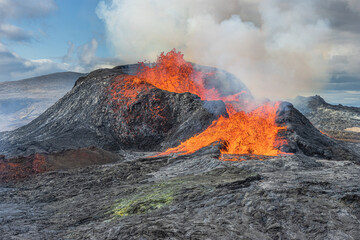 Volcano on Iceland's Reykjanes Peninsula. Lava fountains from the volcanic crater. Landscape in spring with sunshine. Liquid lava flows out of the side of the crater. Strong steam rises from crater