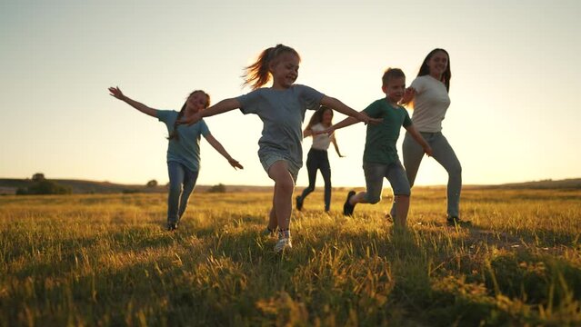 Happy family of children in summer outdoors.Children run together on grass in meadow.Silhouette of group of people playing in field.Boys and girls have fun run in the park at sunset.The Joy of Friends