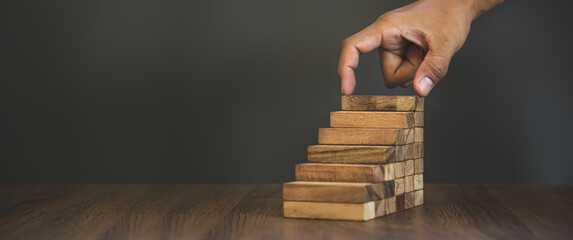 Hand placing wooden block tower stack in pyramid stair step with caution to prevent collapse or...