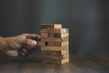 Hand placing wooden block tower stack in pyramid stair step with caution to prevent collapse or crash concepts of financial risk management and strategic planning and business challenge plan.