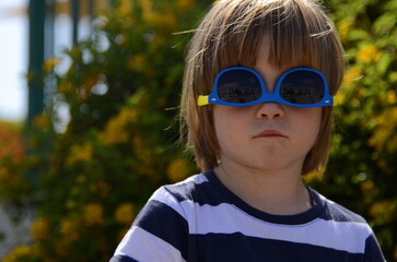 Portrait of a little boy in sunglasses. A child in front of a flowering bush. Concept: holidays, summer camp, kindergarten, family vacation, childhood. Funny kid