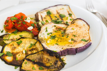 Seasonal grilled vegetables (verdure grigliate) side dish in italian cuisine, slices of eggplant ( courgette), zucchini, and pepper with garlic, olive oil, and parsley.