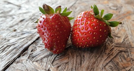 Nahaufnahme von zwei reifen Erdbeeren auf einem Holzbrett