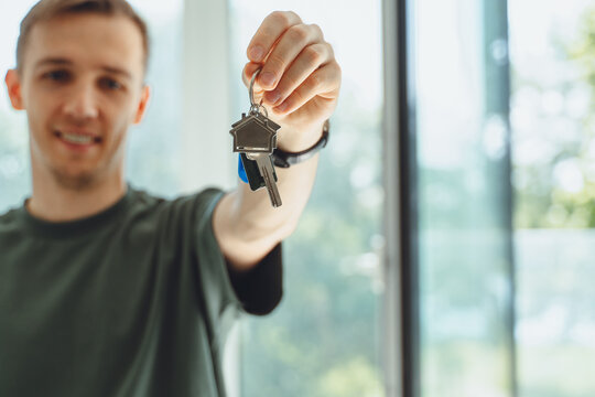 Focus on keys, held by excited young millennial homeowners. Happy single man celebrating moving in new house home, demonstrating keys, standing in apartment, real estate mortgage concept..