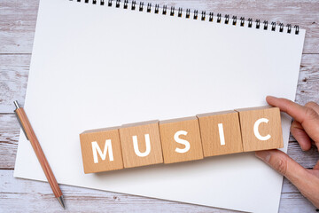 音楽のイメージ｜「MUSIC」と書かれたブロック、ノート、ペン、手